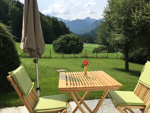 A wooden table with a vase of flowers, two chairs, and an umbrella in a grassy outdoor area with a mountain view. - Bergblick Riedlern, Kreuth Riedlern - Mountain View Riedlern - Apartment (Kreuth)
