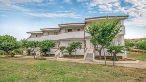 Ein mehrstöckiges Wohngebäude mit weißer Fassade, mehreren Balkonen und einem begrünten Garten mit verschiedenen Bäumen.