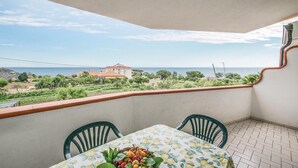Ein Balkon mit Tisch und Stühlen mit Blick auf eine Küstenlandschaft, in der Ferne ein Gebäude.
