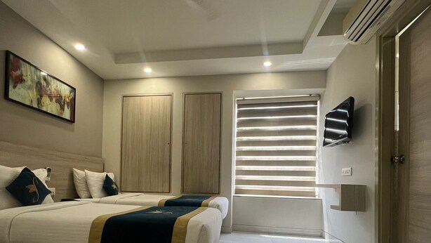 Une chambre d’hôtel moderne dotée d’un grand lit, d’un ventilateur de plafond, d’une télévision et d’une fenêtre avec des stores.