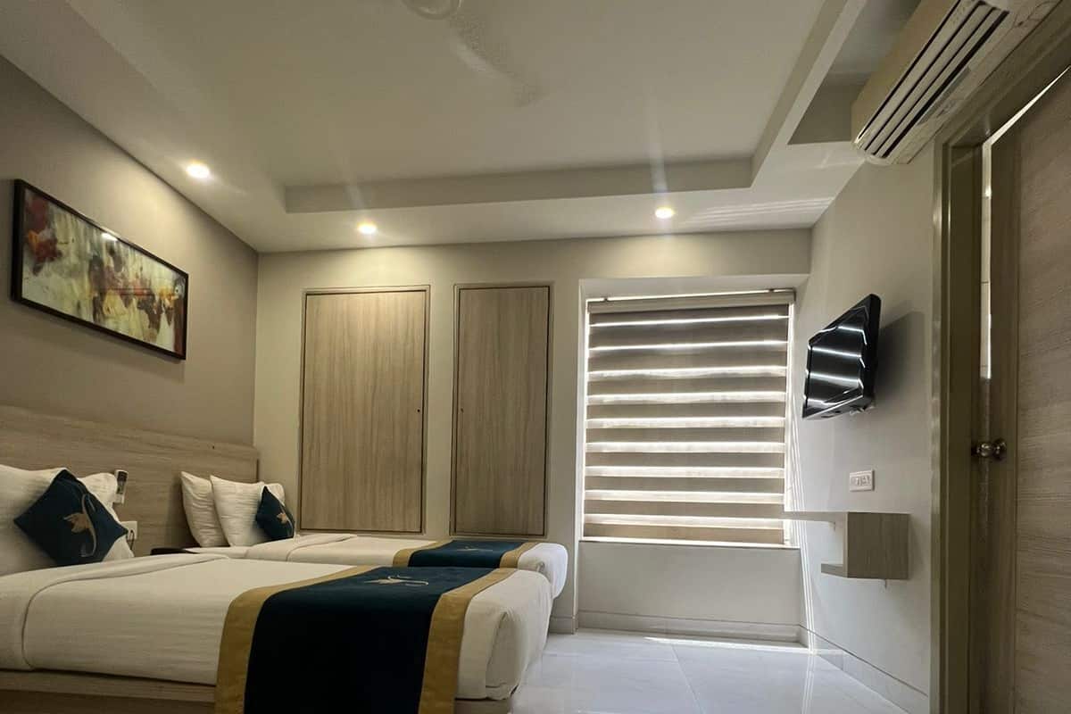 A modern hotel room with a large bed, a ceiling fan, a TV, and a window with blinds.
