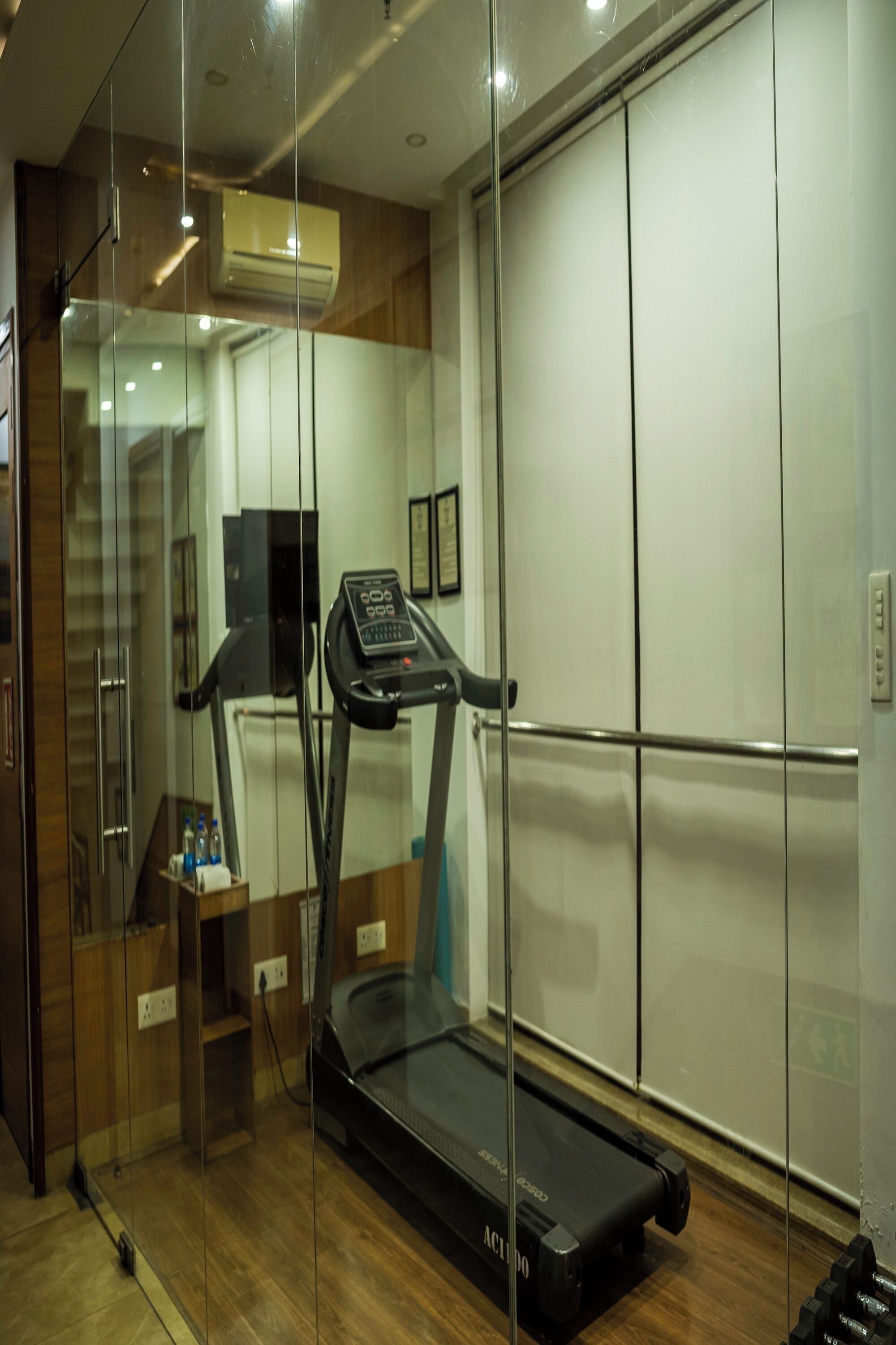 A modern hotel room with a glass partition, a treadmill, and a wooden floor.