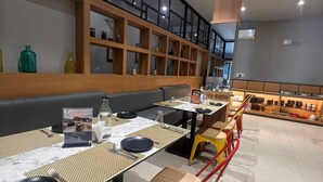 Un intérieur de restaurant moderne avec des tables hautes, des banquettes rembourrées et une variété d’objets décoratifs disposés sur des étagères.