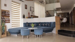 Un salon moderne avec un canapé bleu, deux poufs assortis, une petite table ronde ornée d’un vase et un escalier menant à un niveau supérieur.