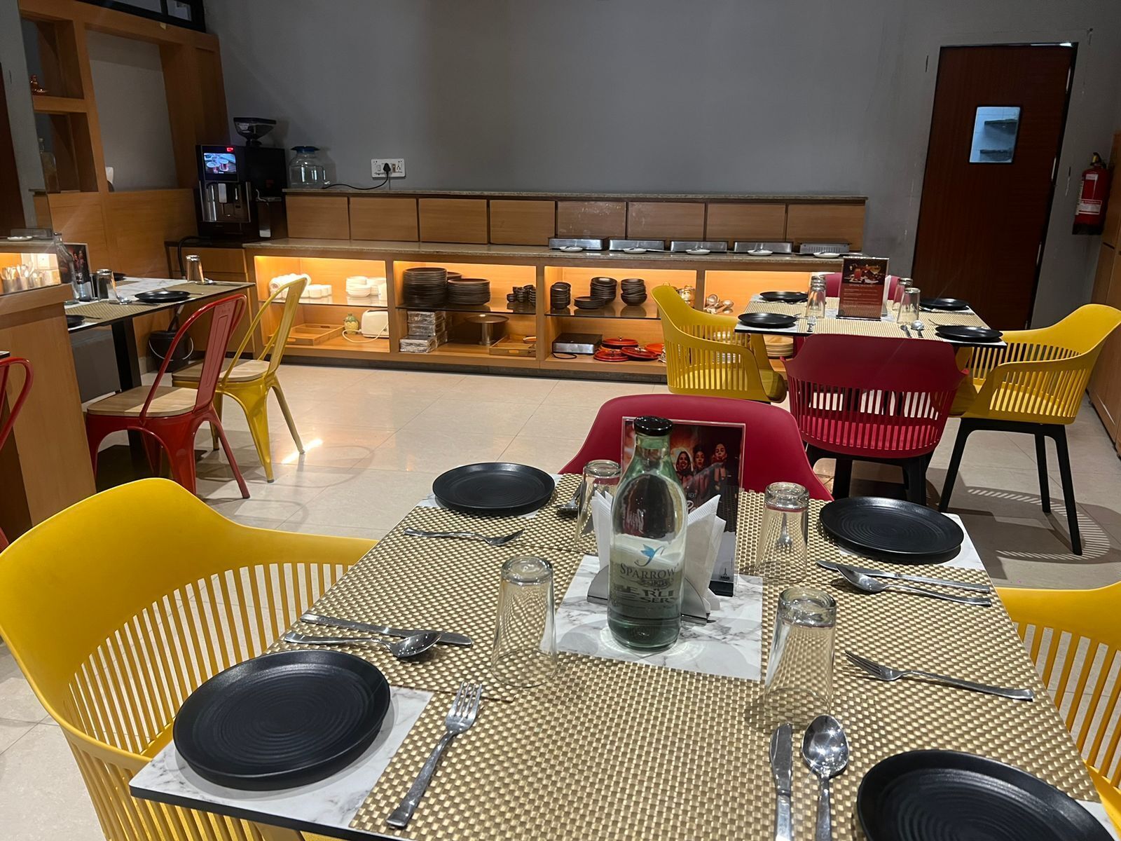 Un restaurante con mesas dispuestas para comer, que presenta distintos tipos de sillas y una vitrina de exhibición al fondo.