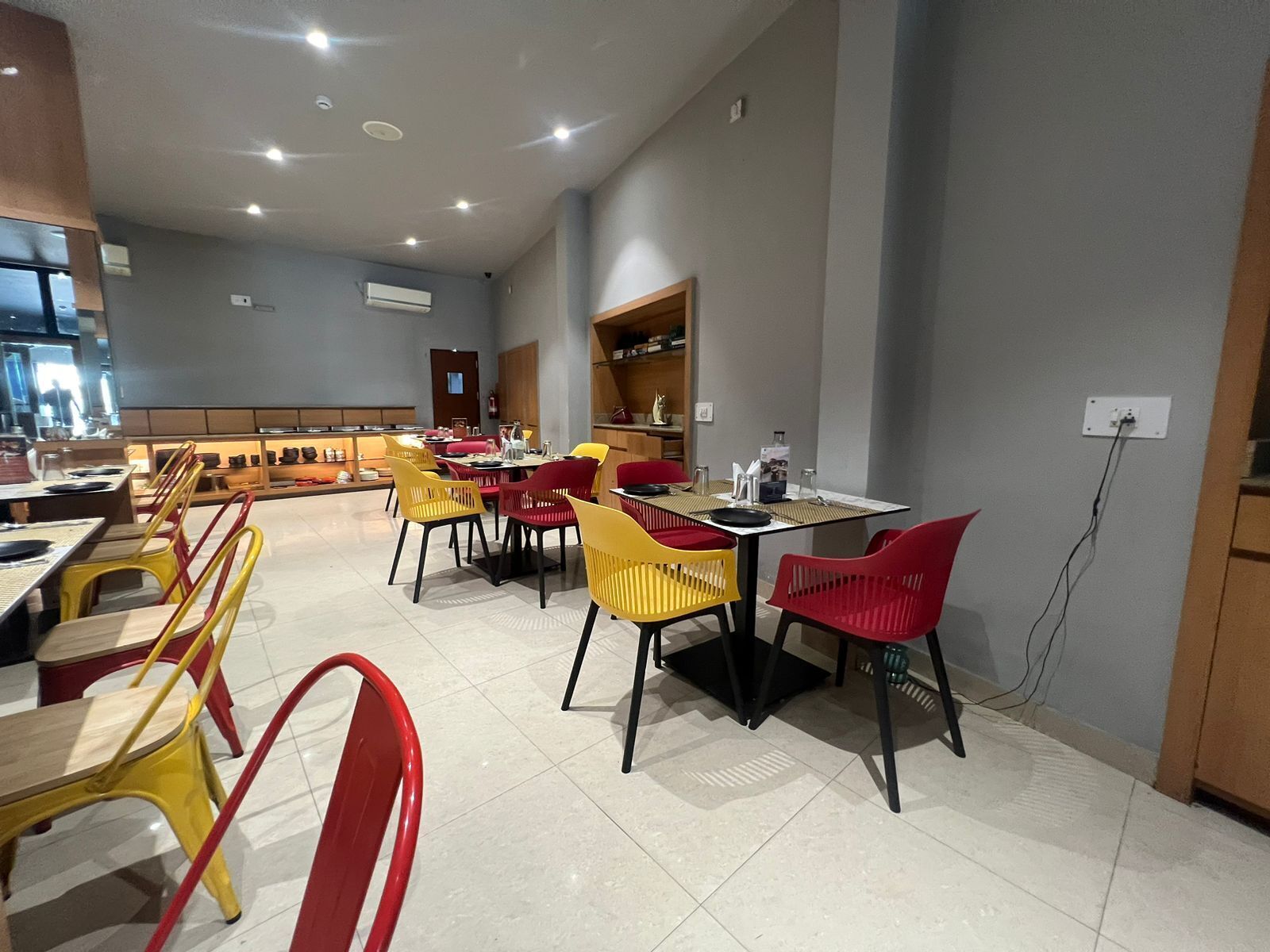 Un espace repas moderne avec plusieurs tables et chaises, un extincteur bien visible et une prise électrique au mur.
