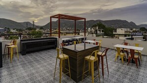 Une terrasse sur le toit avec un sol à motifs, une table centrale entourée de chaises et une structure en forme de pergola.
