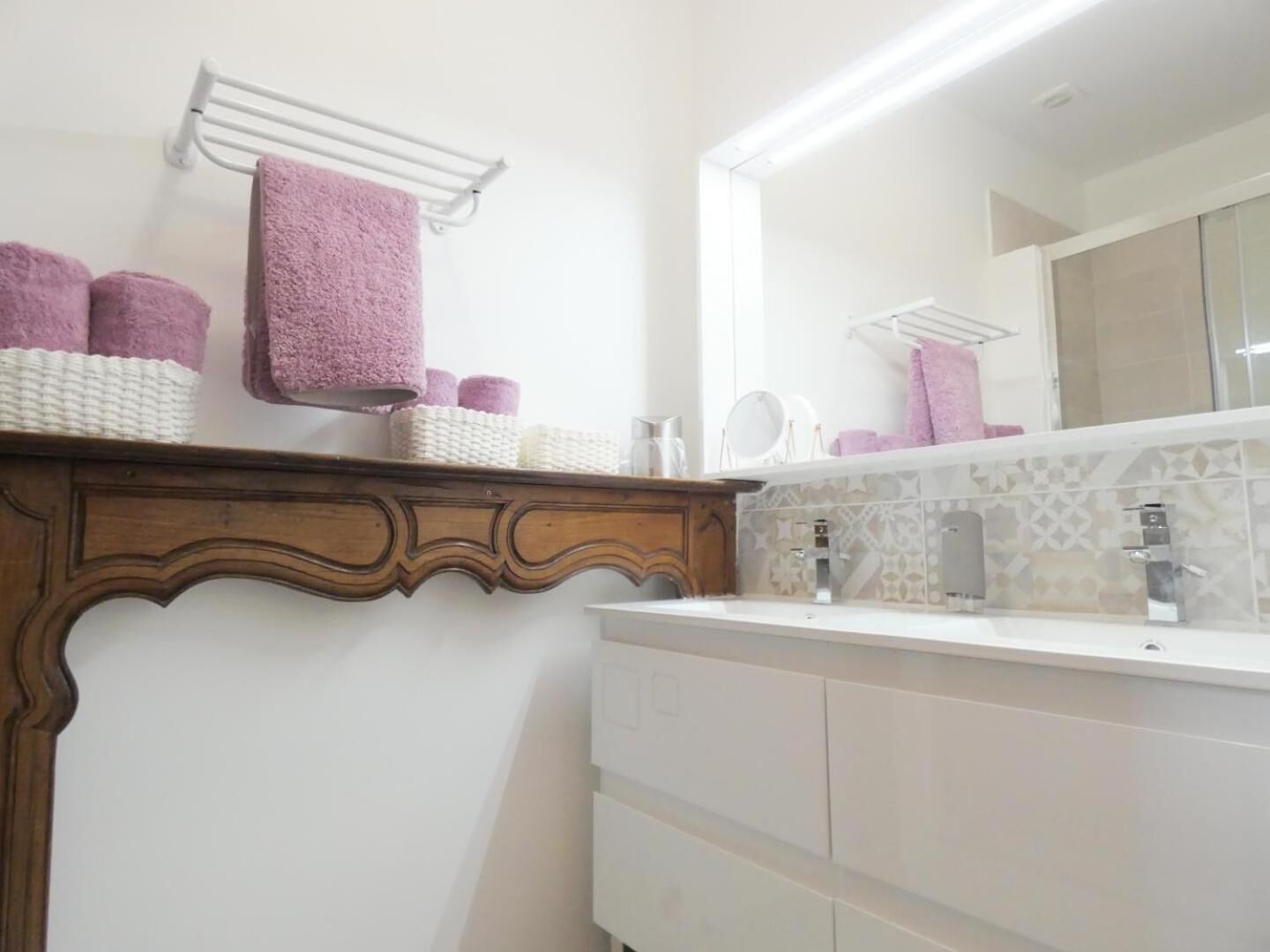 Une salle de bain avec un meuble-lavabo en bois, un miroir et une étagère où sont rangées les serviettes et les articles de toilette.