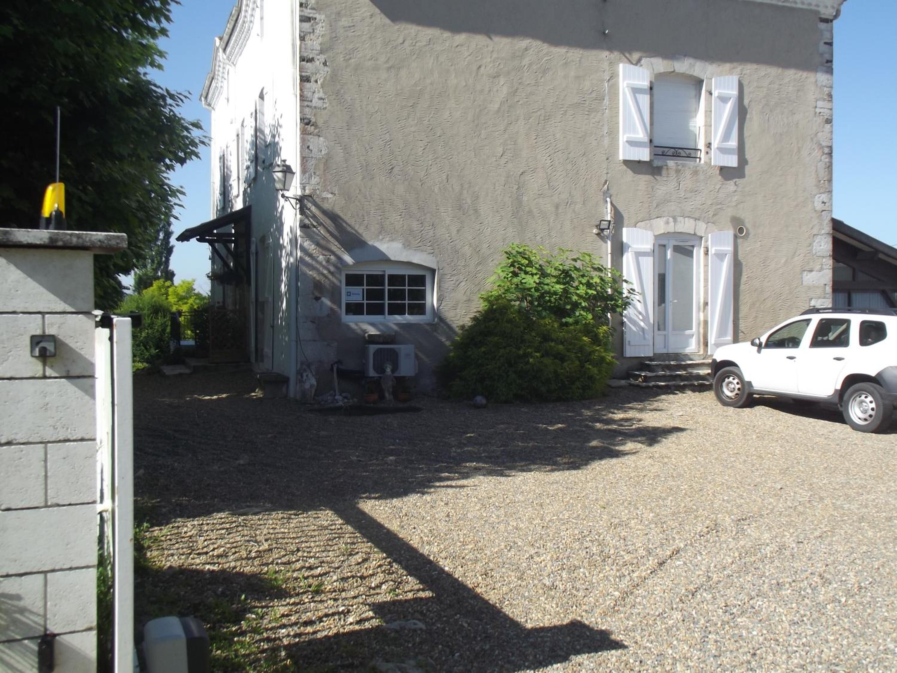 A building with a gravel driveway, a white car parked in front, and a small garden area.