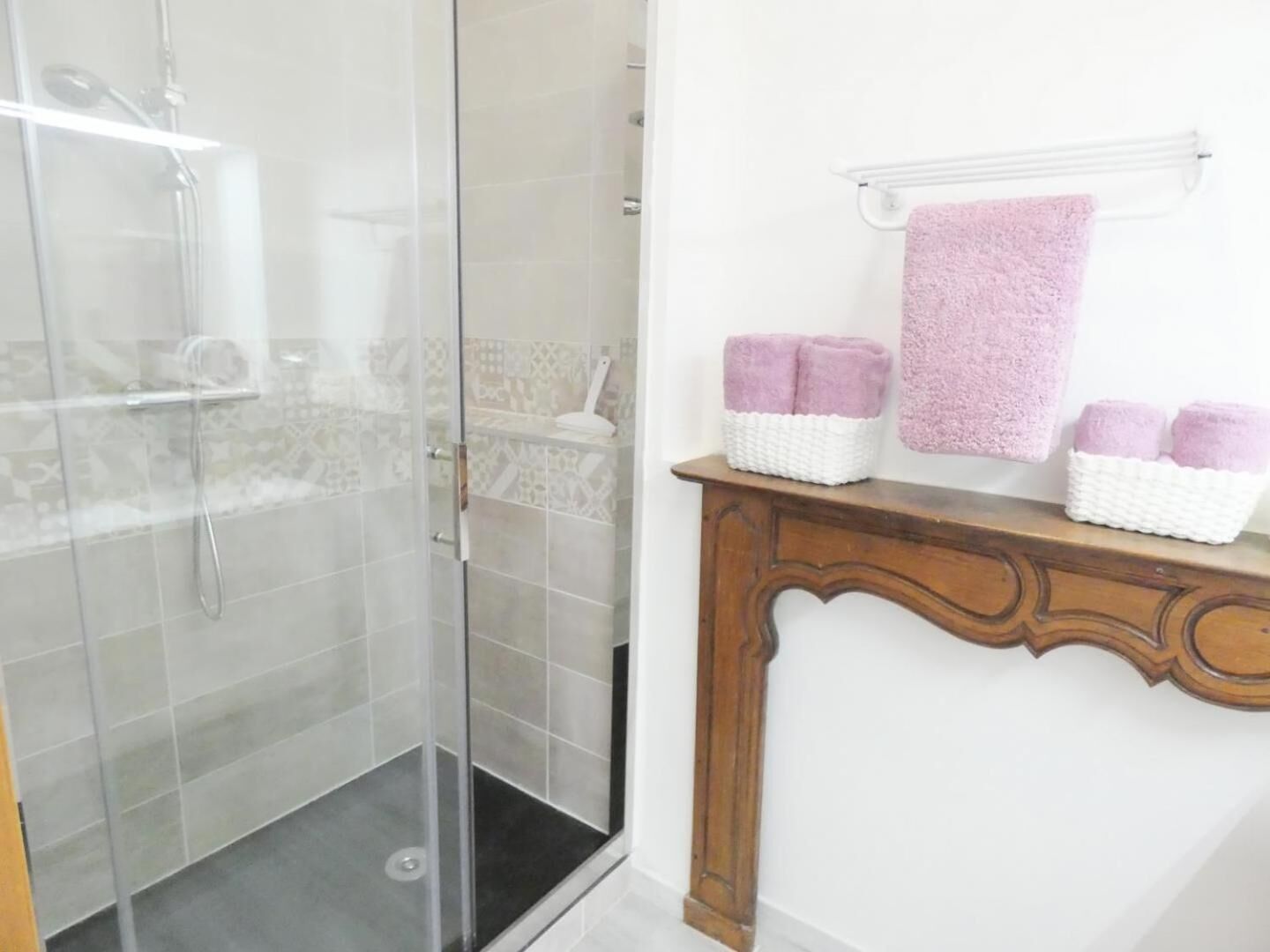 Un bagno con box doccia in vetro, un mobile bagno in legno con specchio e uno scaffale con asciugamani.