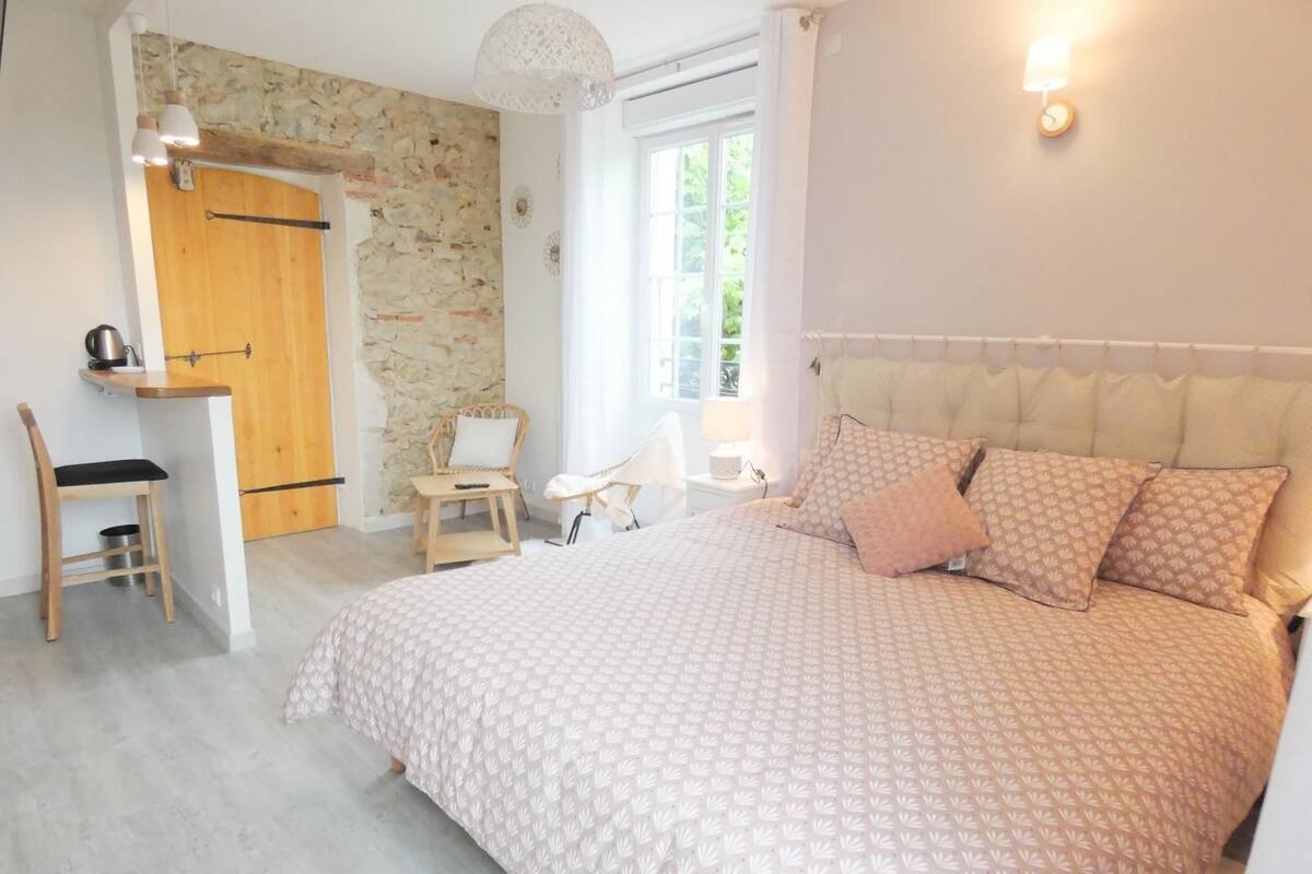 Une chambre avec un grand lit, un bureau en bois, une chaise et un mur en pierre.