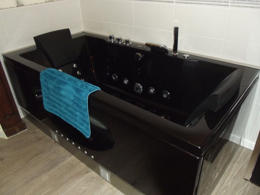 A black bathtub with multiple controls and a blue towel.