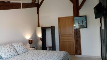 A bedroom with a bed, a wooden door, a mirror, a wall-mounted TV, and a framed picture.