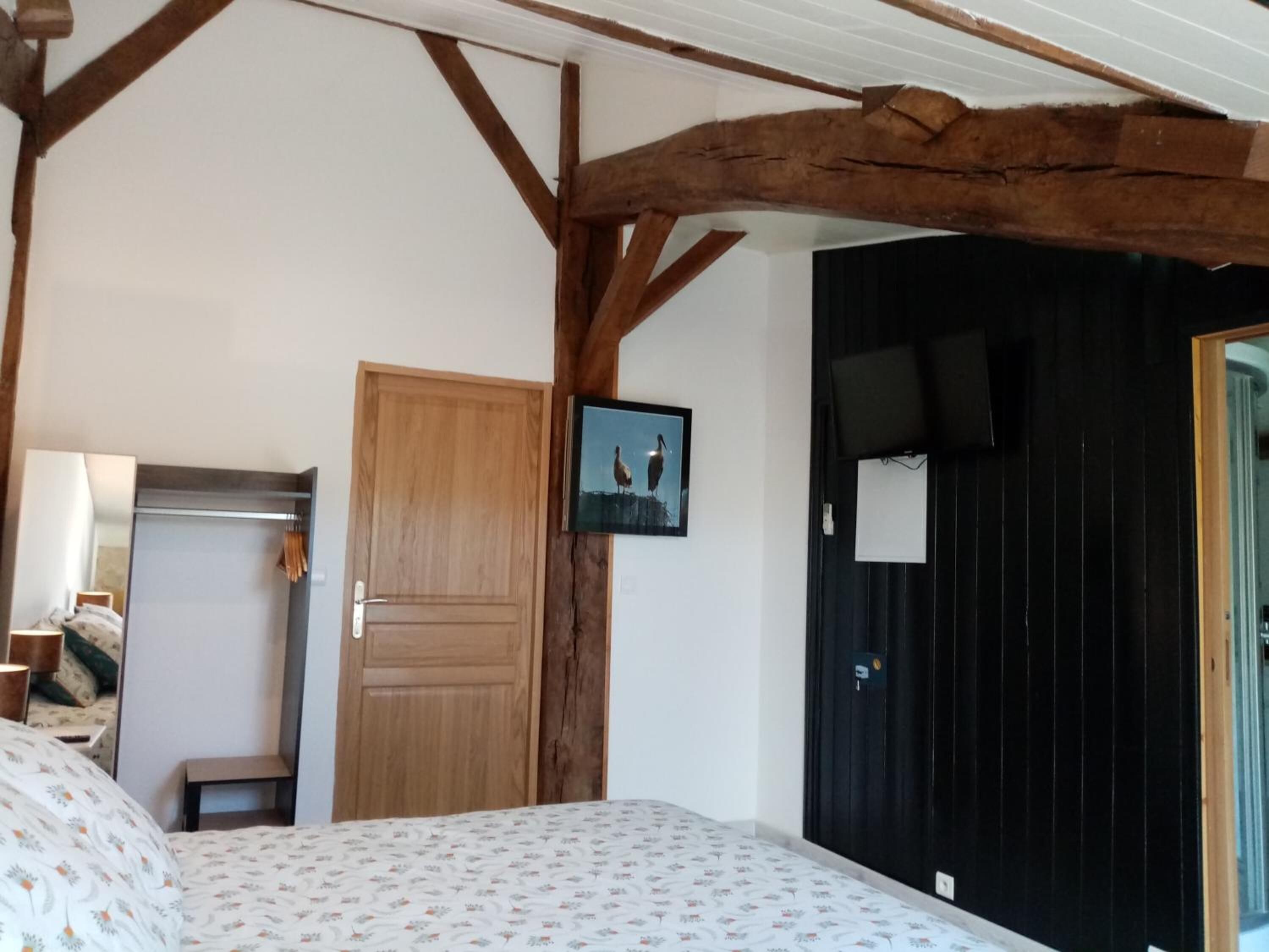 Un dormitorio con techo de madera, una cama con ropa de cama floral, una puerta de madera, una mesita de noche pequeña y un cuadro enmarcado en la pared.