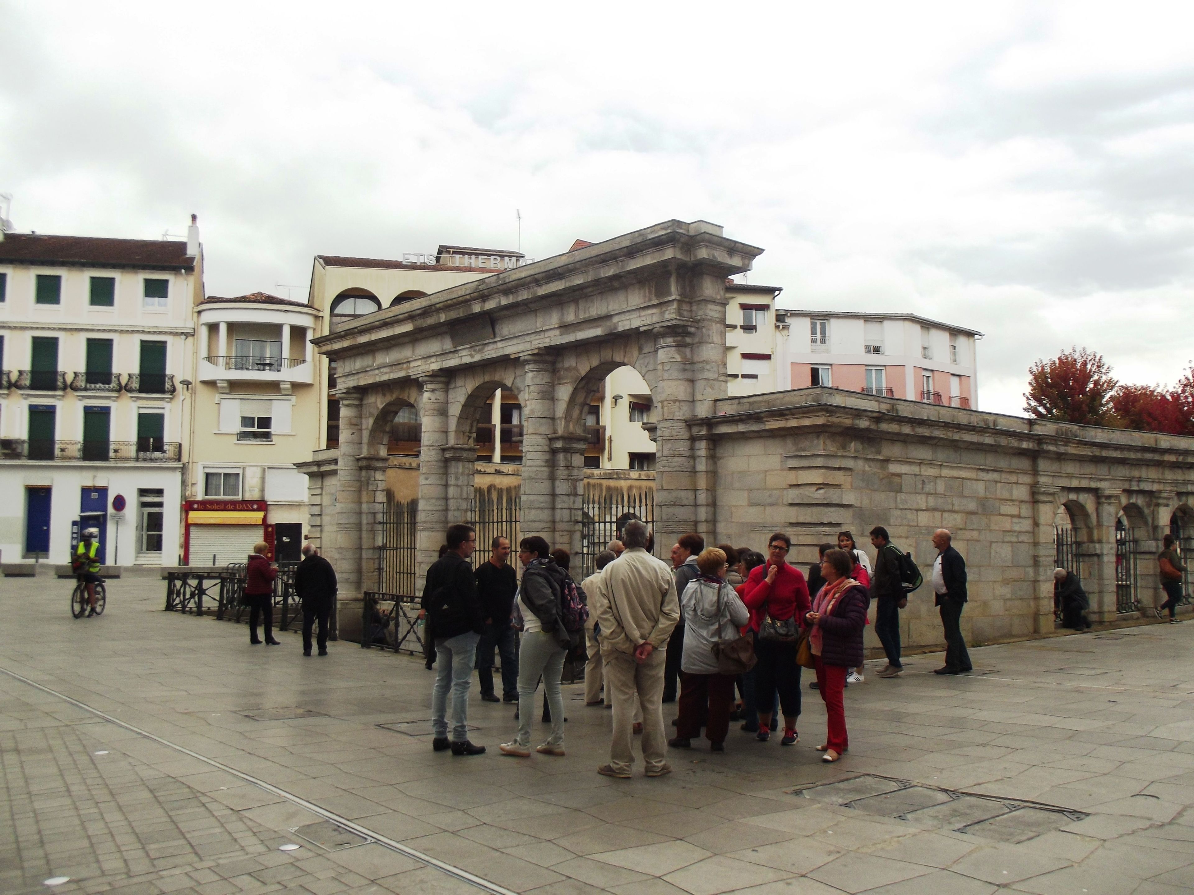 A group of people gathered in front of a historic building with classical architecture, including arches and columns.