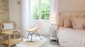 A bedroom with a bed, a chair, a nightstand, and a window.
