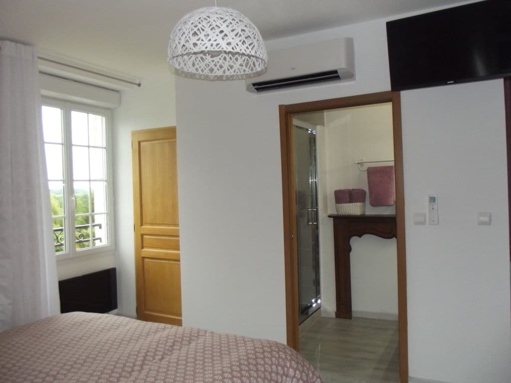 A bedroom with a bed, a wooden wardrobe, a mirror, and a window.