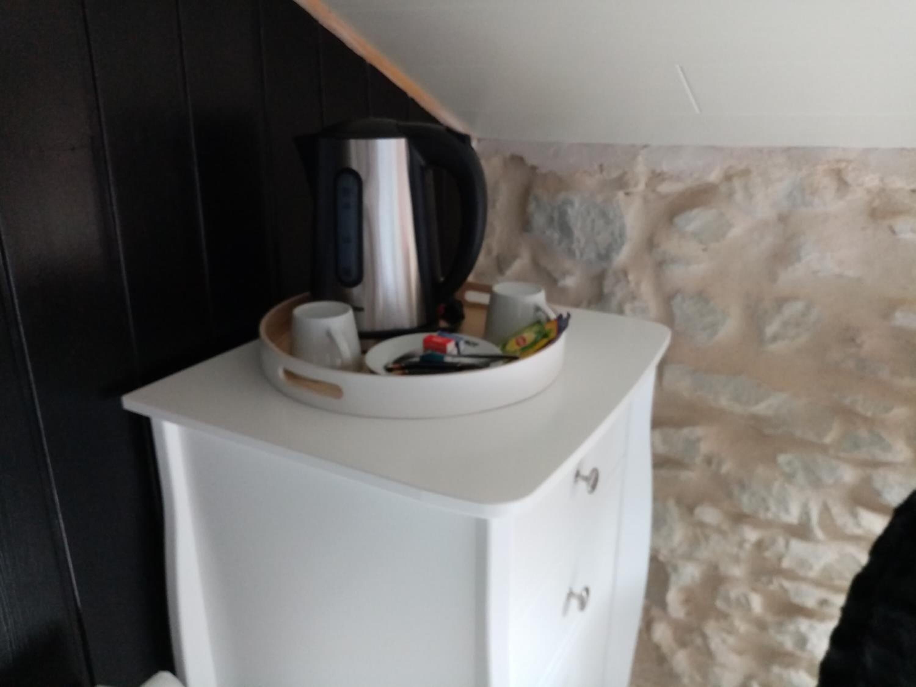 Ett litet pentry med ett vitt skåp, en vattenkokare, en mugg och en skål med snacks.