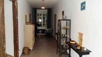Un couloir étroit avec un plancher en bois, une chaise noire, une petite table avec une lampe et une vitrine contenant divers objets.