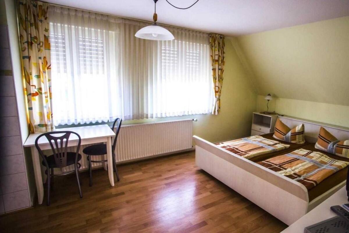A bedroom with a bed, a desk, a chair, a TV, and a window with curtains.
