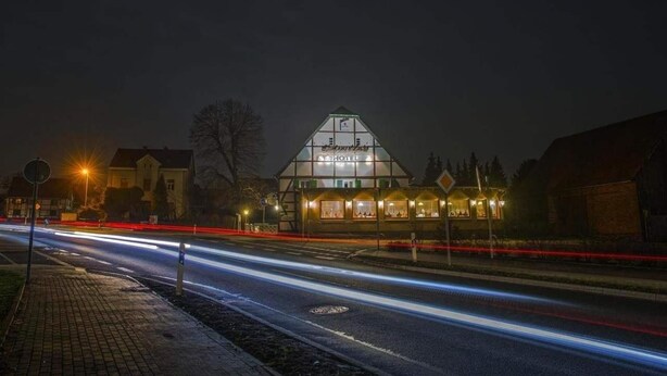 A hotel with a prominent sign, a well-lit facade, and a clear view of the road with light trails. - Lindenschänke Hotel garni (Werl)