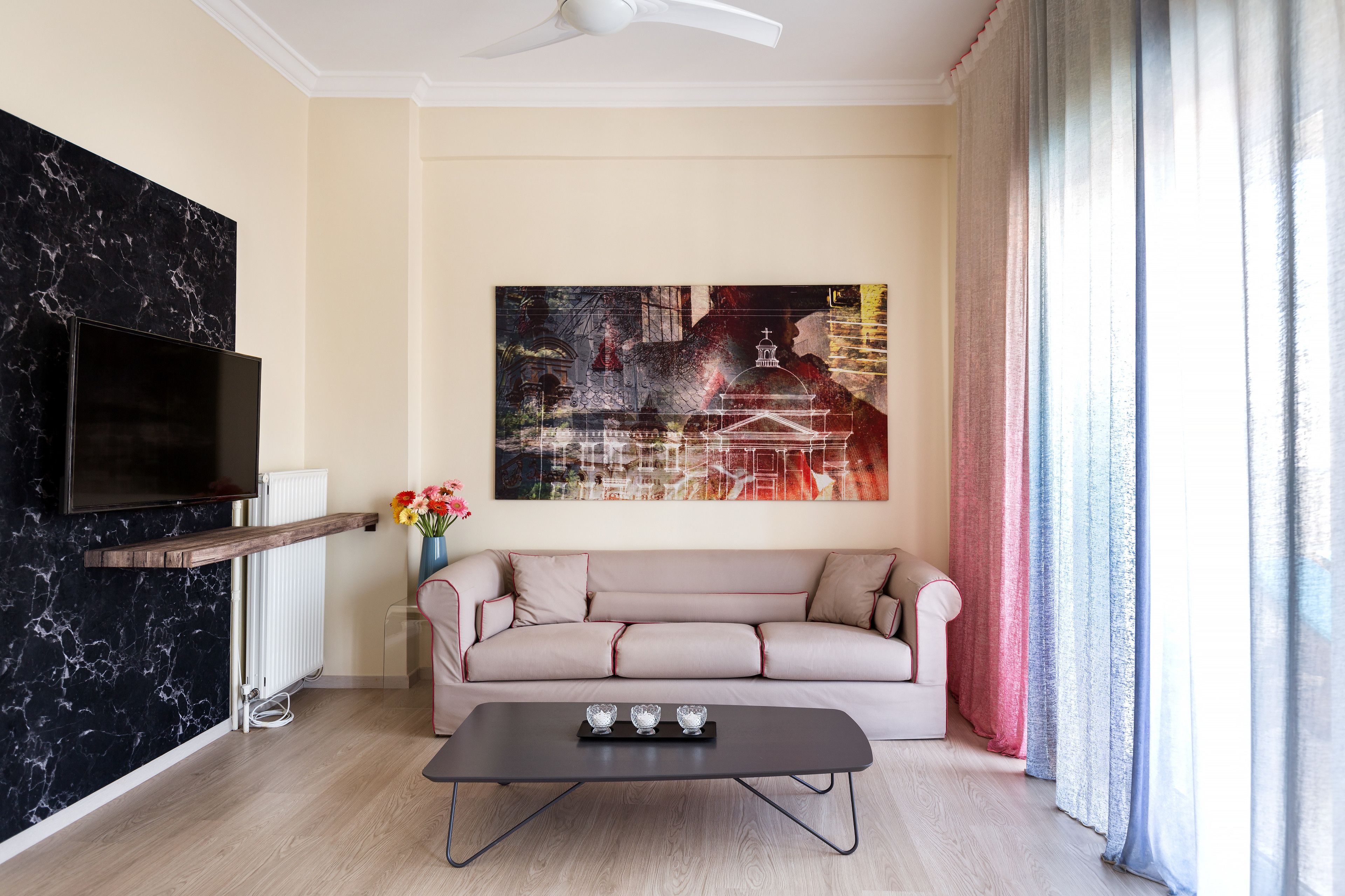 Een woonkamer met een televisie met zwarte lijst, een beige bank, een salontafel en een groot abstract schilderij aan de muur.