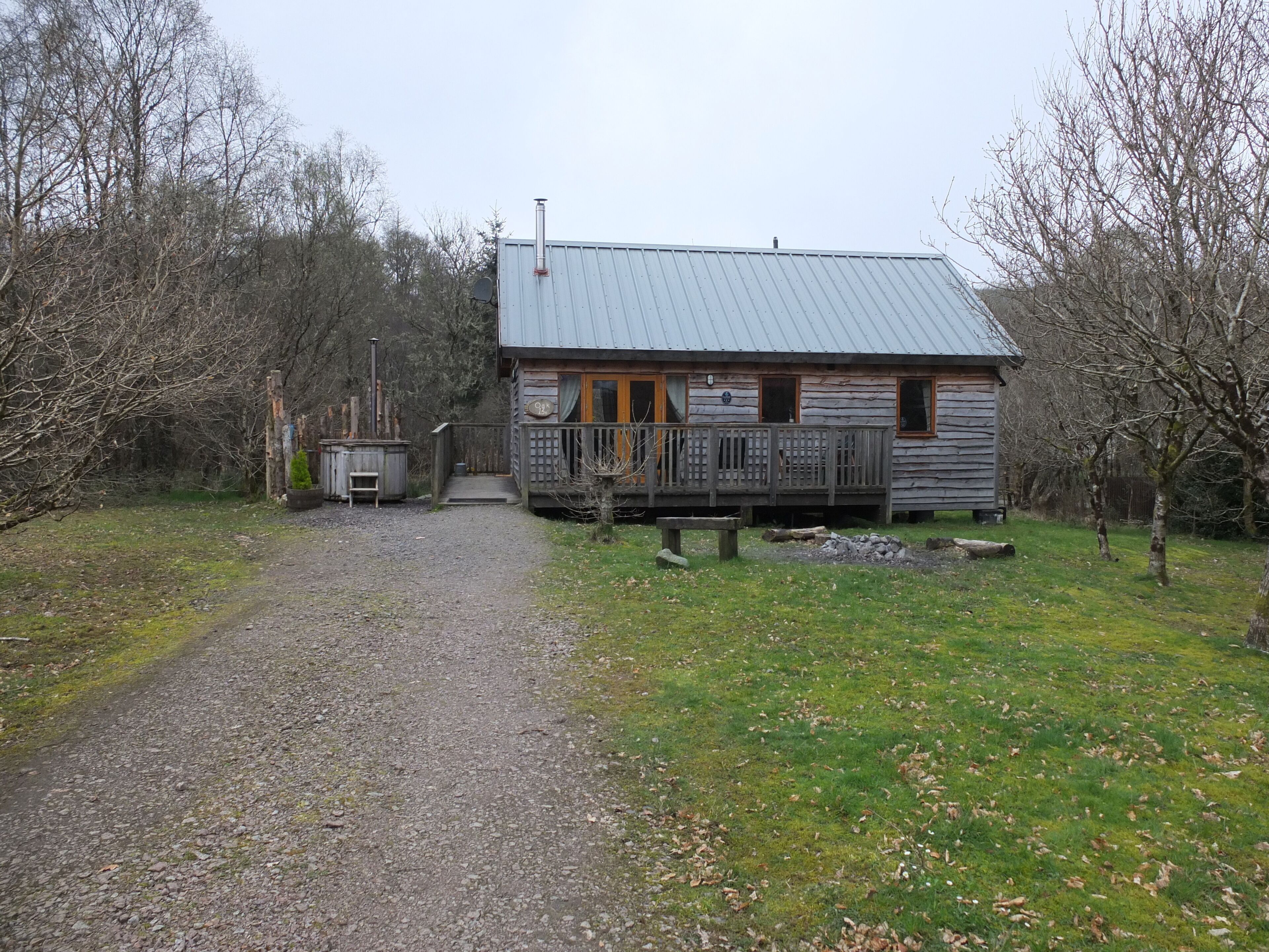 Un chalet rustique, avec un chemin de gravier menant à l’entrée, entouré d’arbres.