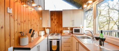 Een compacte keuken met houten wanden, een fornuis, een magnetron en een spoelbak.