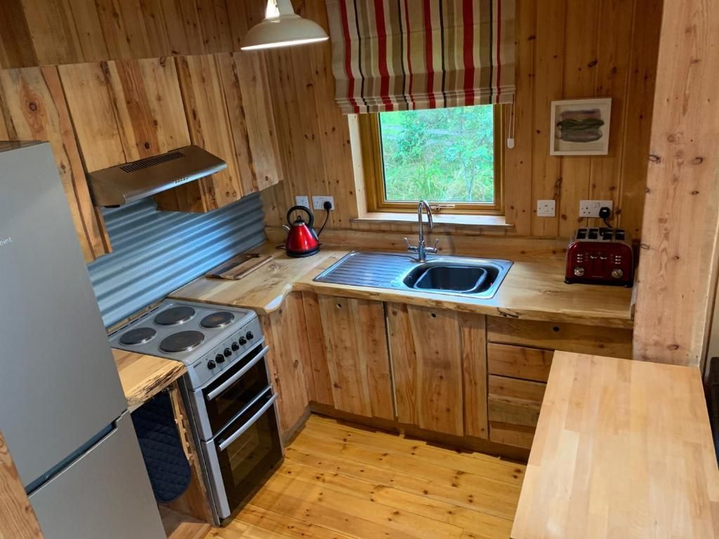 A compact kitchen with wooden cabinets, a stainless steel stove, a sink, and a window with a view of greenery.