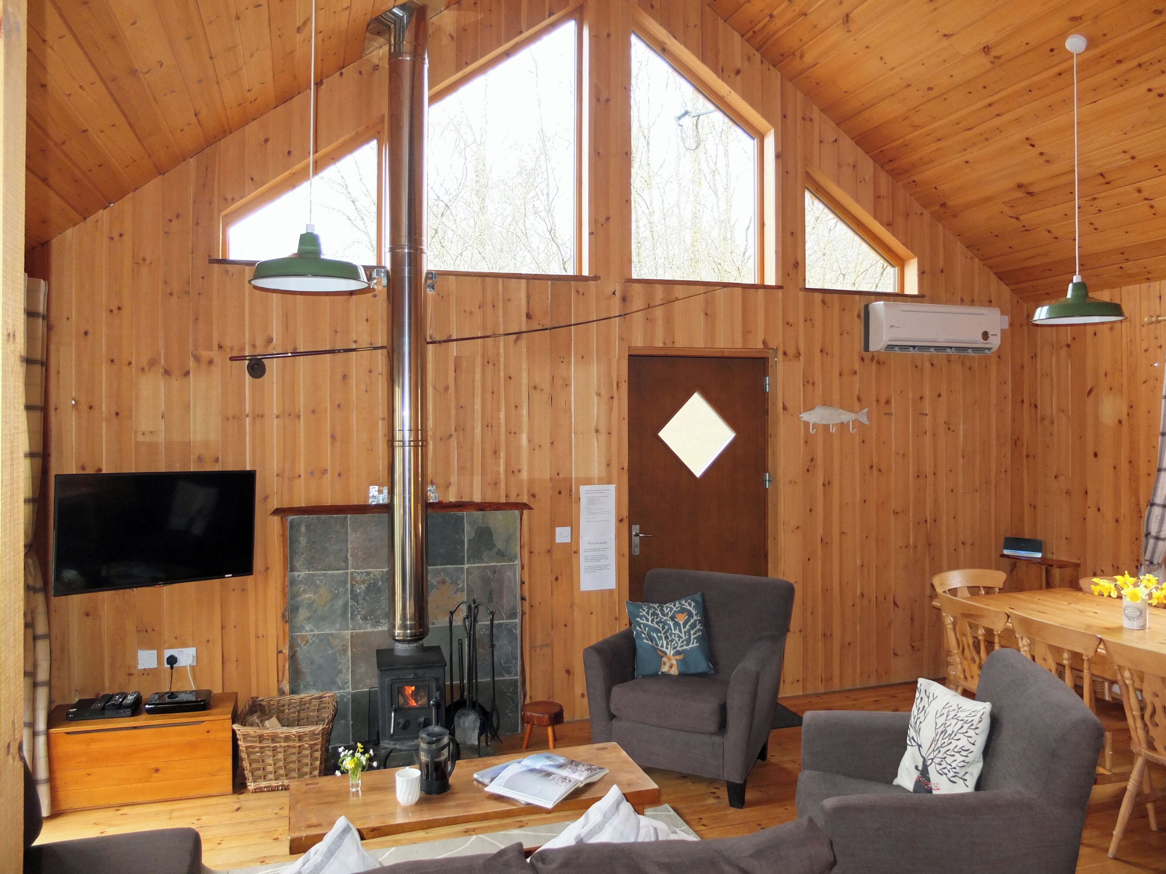 A wooden cabin interior with a fireplace, wooden walls, a television, and a dining area.