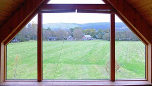 Una habitación con un amplio ventanal triangular que ofrece vistas a un campo verde y edificios lejanos.