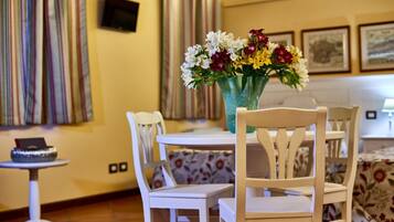 A dining area with white chairs and a round table, a vase with flowers, and a small table with a book and a decorative item.
