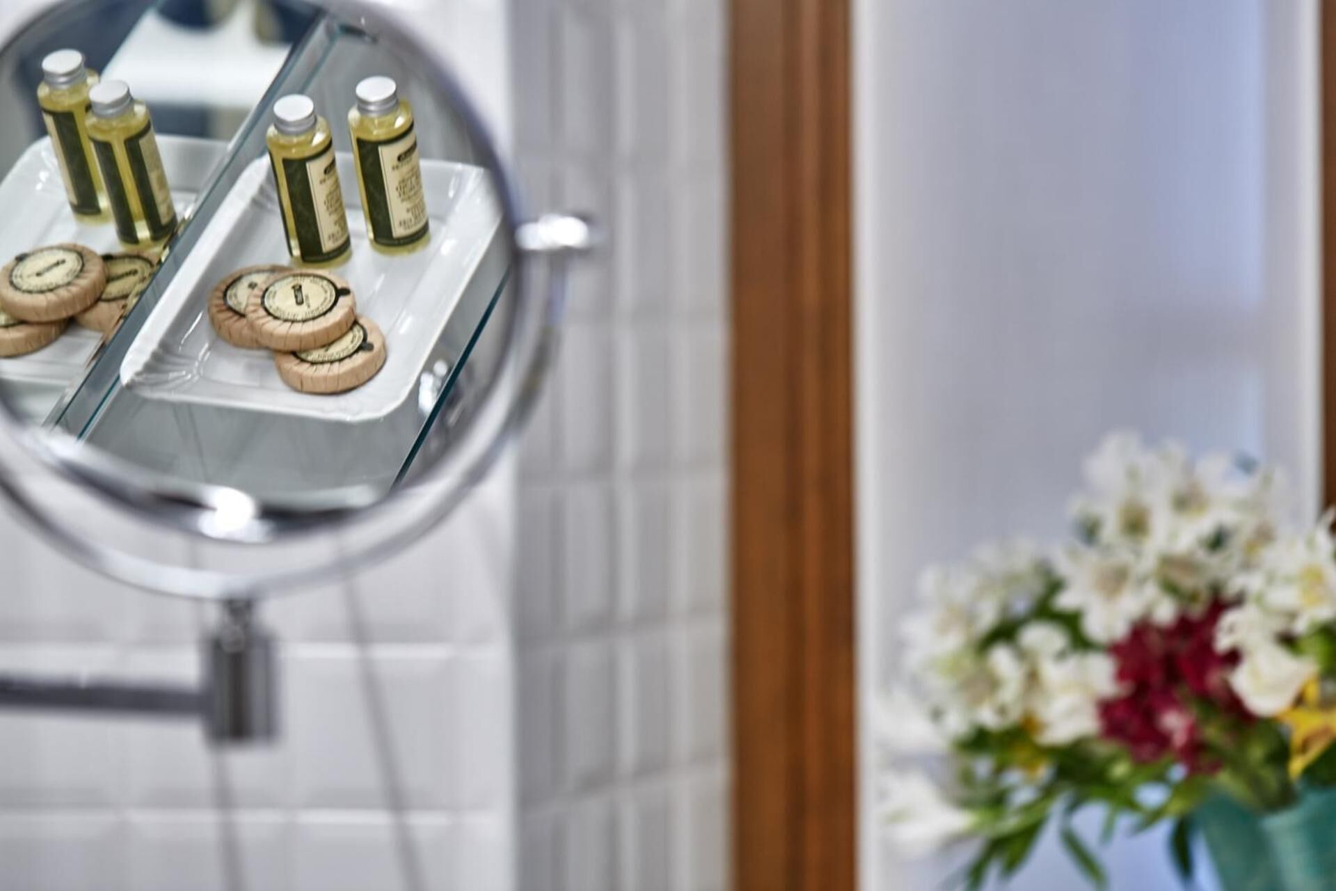 Un tocador de baño con un espejo, una bandeja con artículos de aseo y un florero con flores.