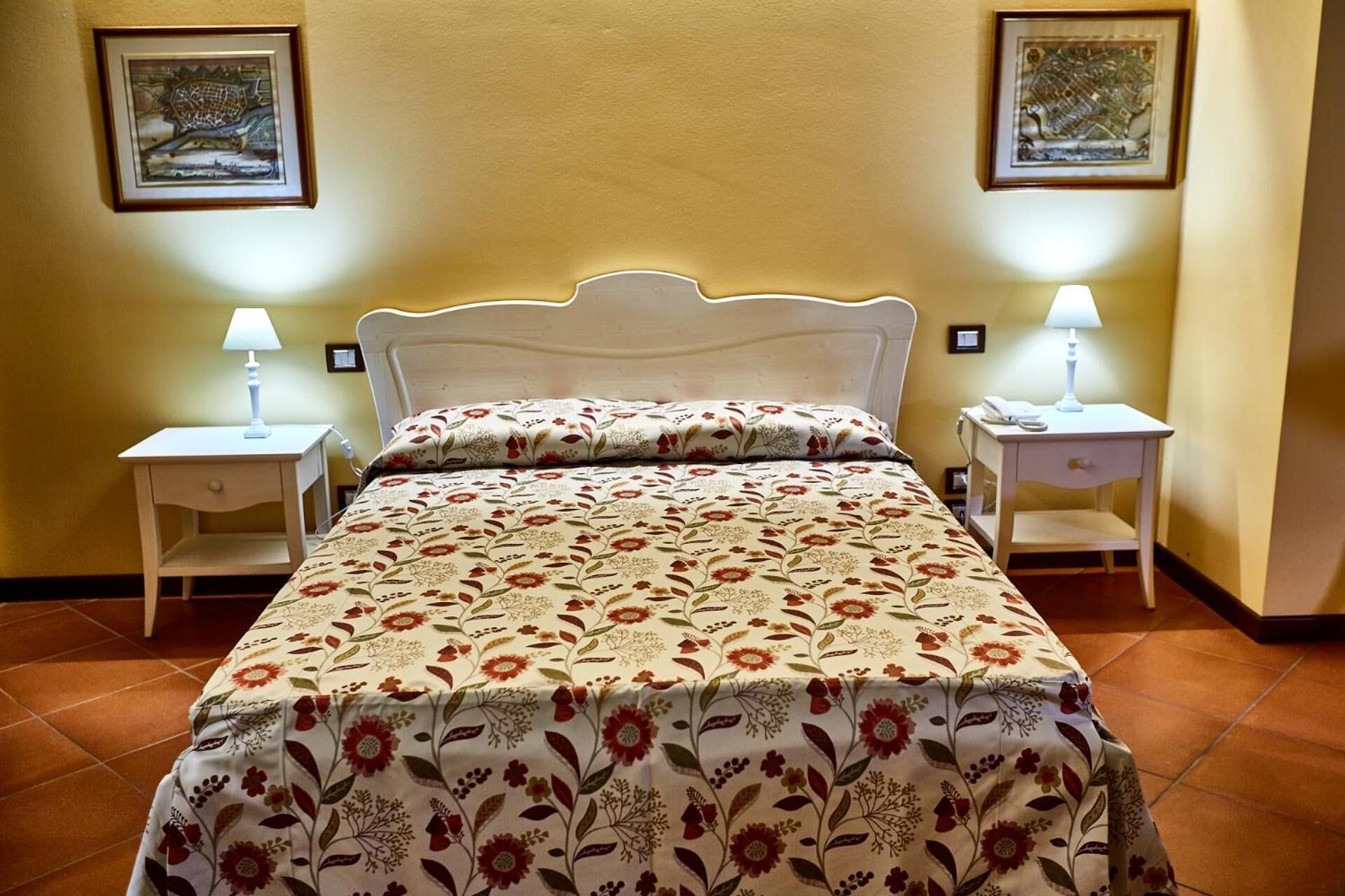 A neatly made bed with floral bedding, two bedside tables with lamps, and two framed pictures on the wall.