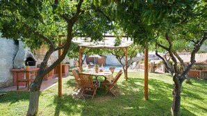 Un área de comedor al aire libre con una pérgola, sillas de madera y una mesa dispuesta para cuatro.