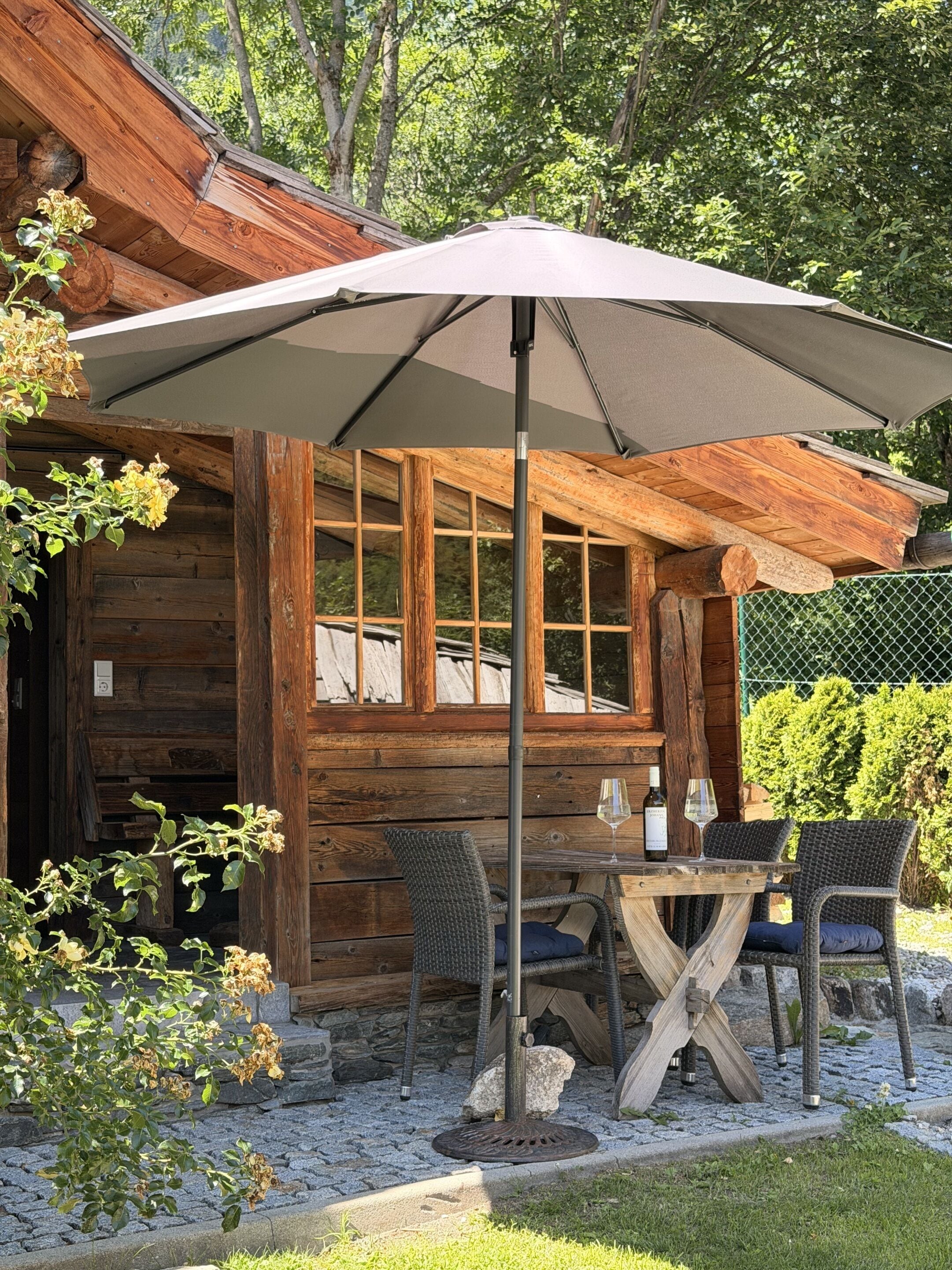 A wooden cabin with a dining area featuring a table and chairs, an umbrella, and a bottle of wine.
