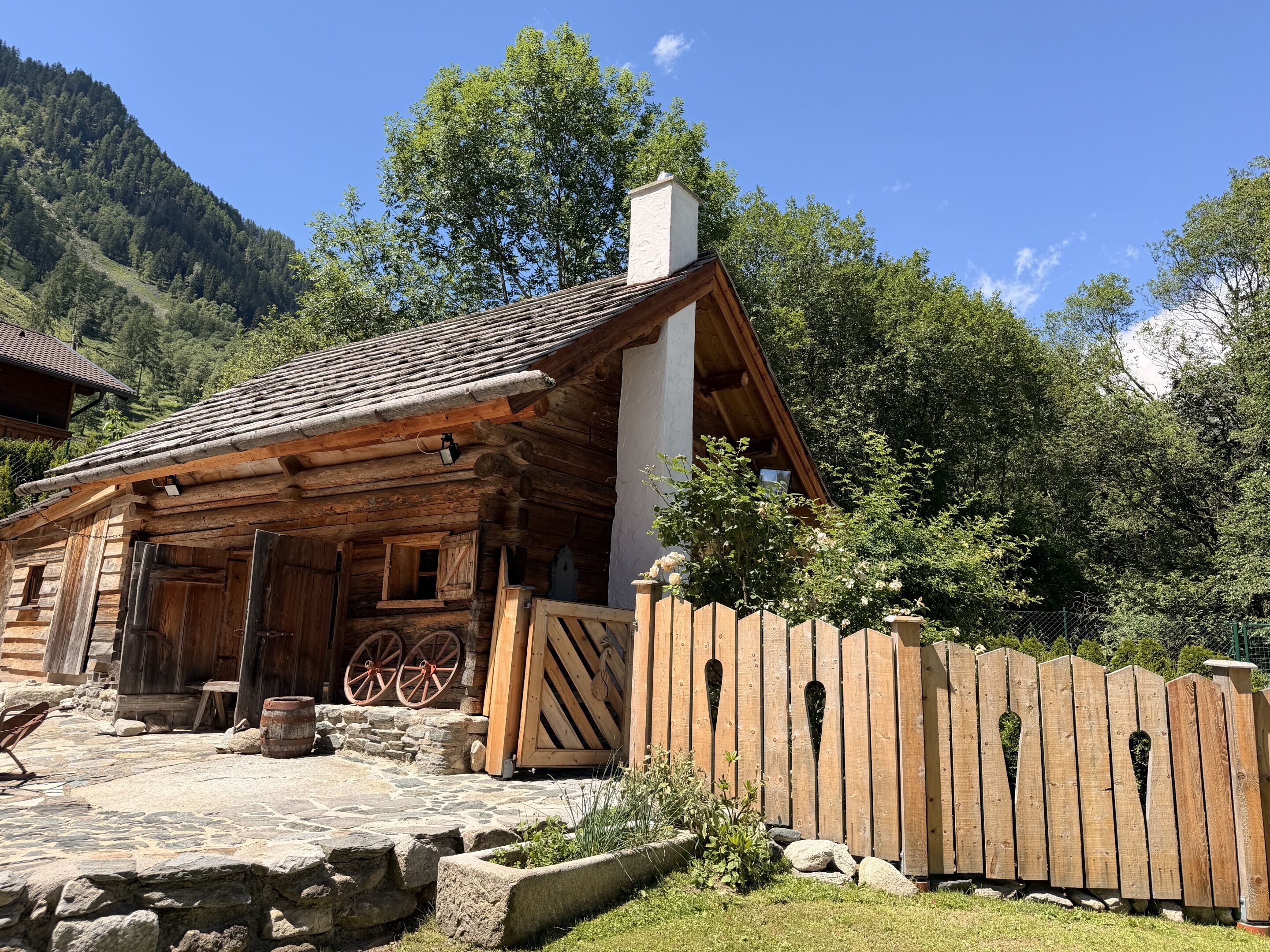 A rustic log cabin with a stone-paved entrance, wooden wheelbarrows, and a wooden fence.