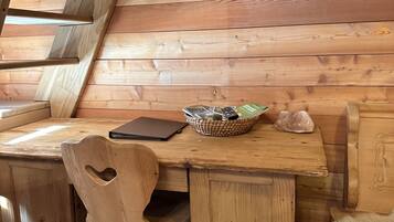 A wooden cabin interior with a loft-style bed, a wooden desk with a laptop, a woven basket, and a deer skull on the wall.