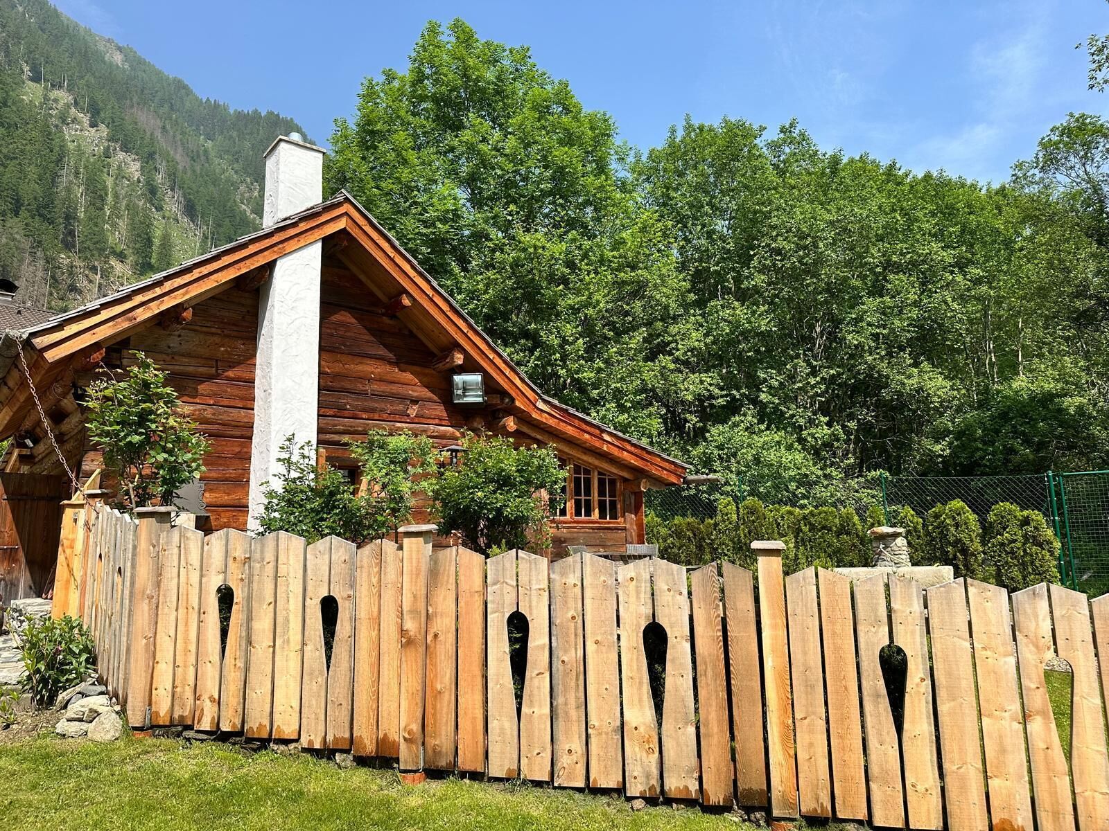 Une cabane en bois avec un toit en pente, entourée d’une clôture en bois ornée de motifs découpés.