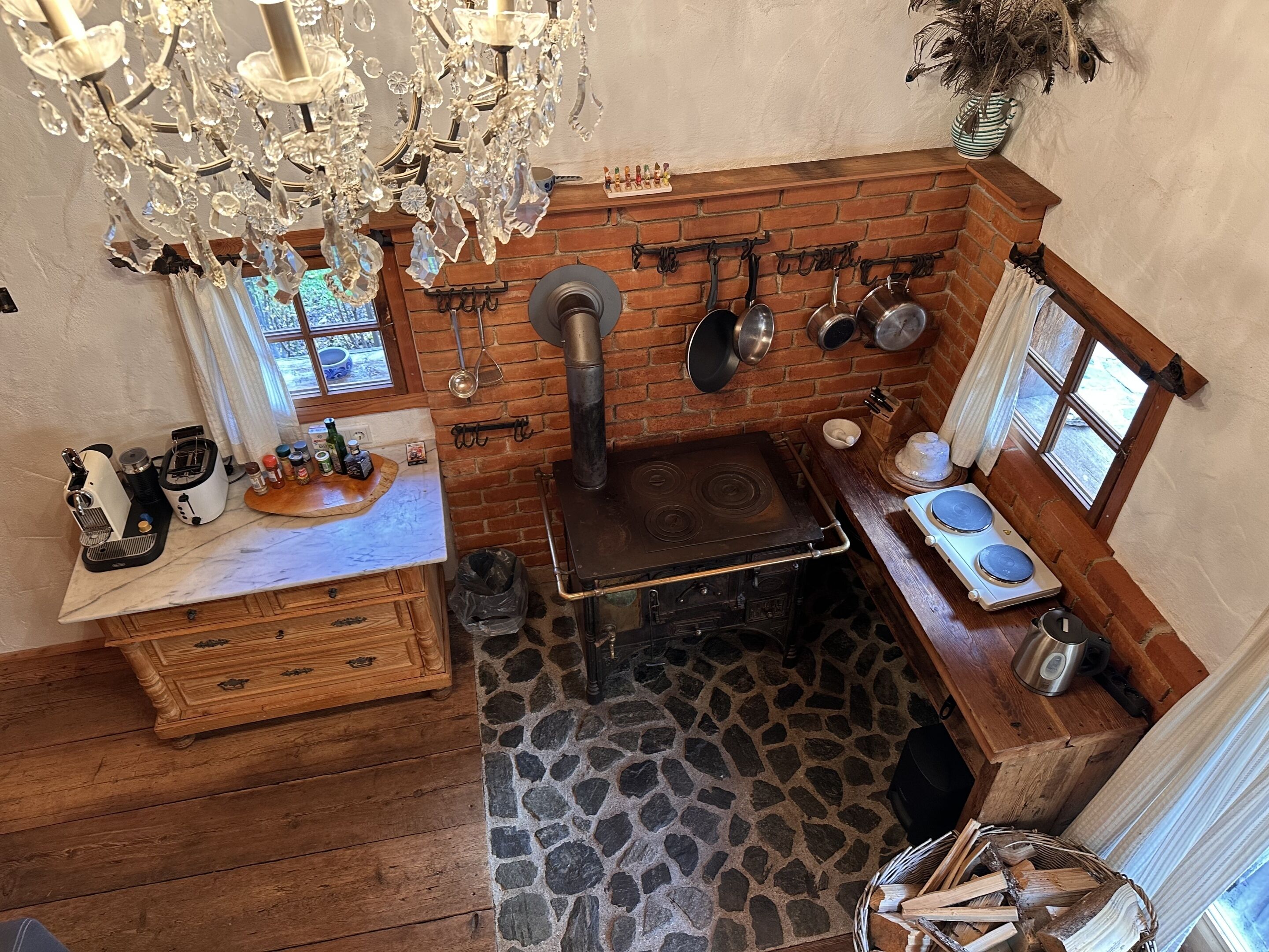 A rustic kitchen with a stone floor, wooden cabinets, a brick wall, and a hanging pot rack.