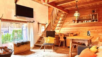 Accogliente interno di una baita in legno con una scala in legno, un'area pranzo e un televisore montato a parete.