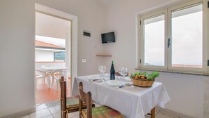 Zona pranzo con tavolo apparecchiato per due, televisione a parete e finestra con vista sul cielo.