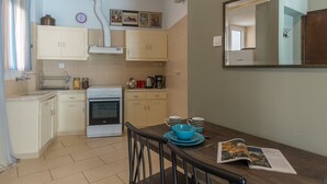 Cocina compacta con armarios blancos, estufa y mesa de comedor con vajilla azul.
