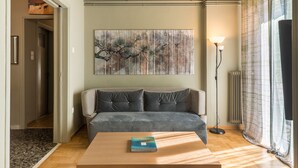 Una sala de estar con un sofá, una mesa de centro con un libro, un cuadro en la pared y una lámpara de pie.