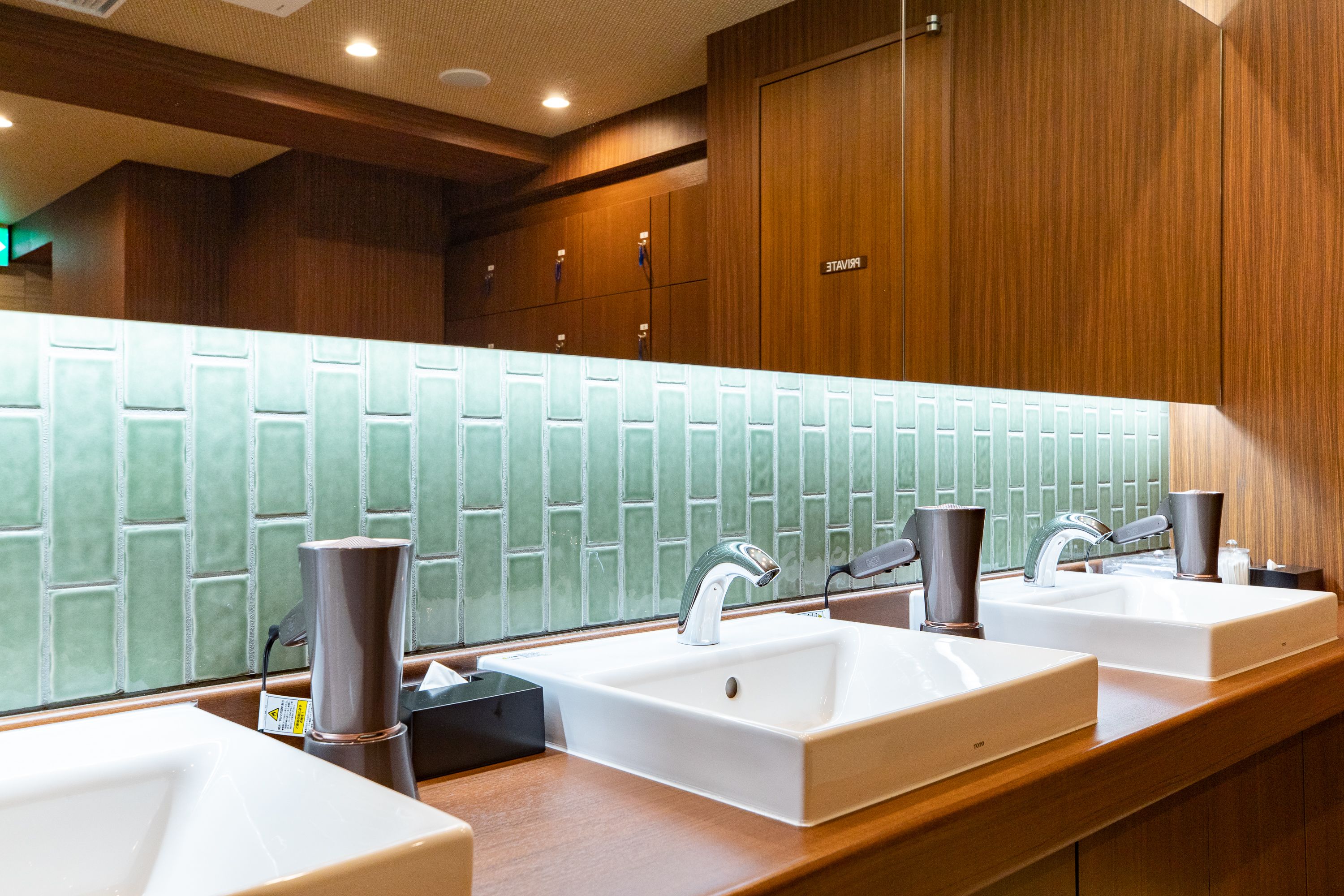 A modern bathroom with two sinks, a mirror, and a green-tiled wall.