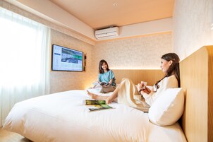 A hotel room with a large bed, a mounted TV, and a wall-mounted air conditioner.