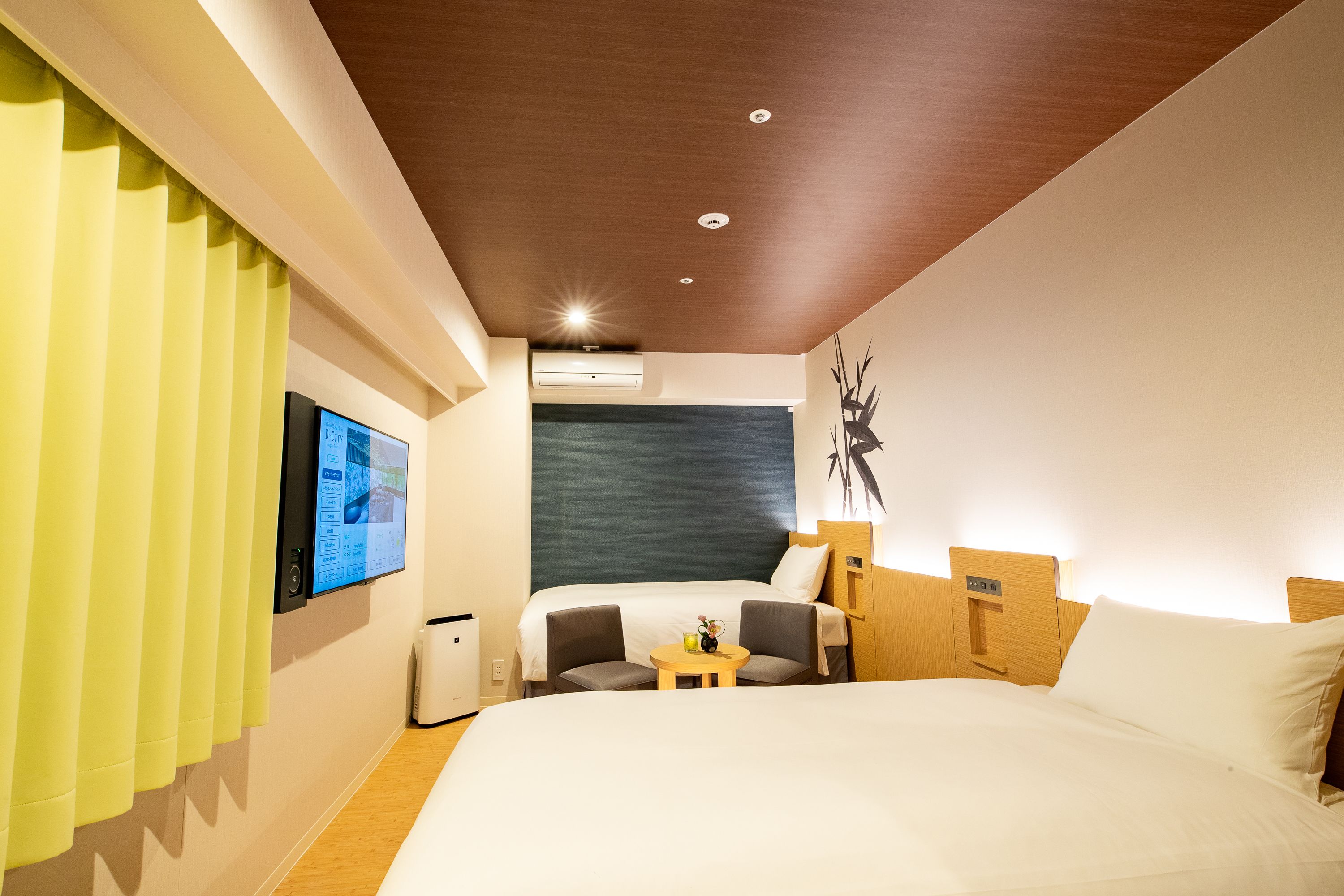 Ein modernes Hotelzimmer mit einem großen Bett, einem kleinen Tisch, zwei Stühlen, einem Fernseher und einer Klimaanlage.