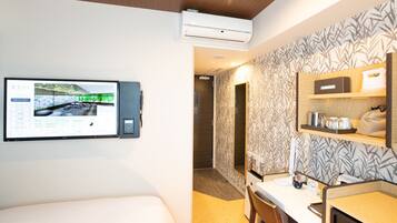 A hotel room with a bed, a desk, a mirror, and a wall-mounted TV displaying a cityscape.
