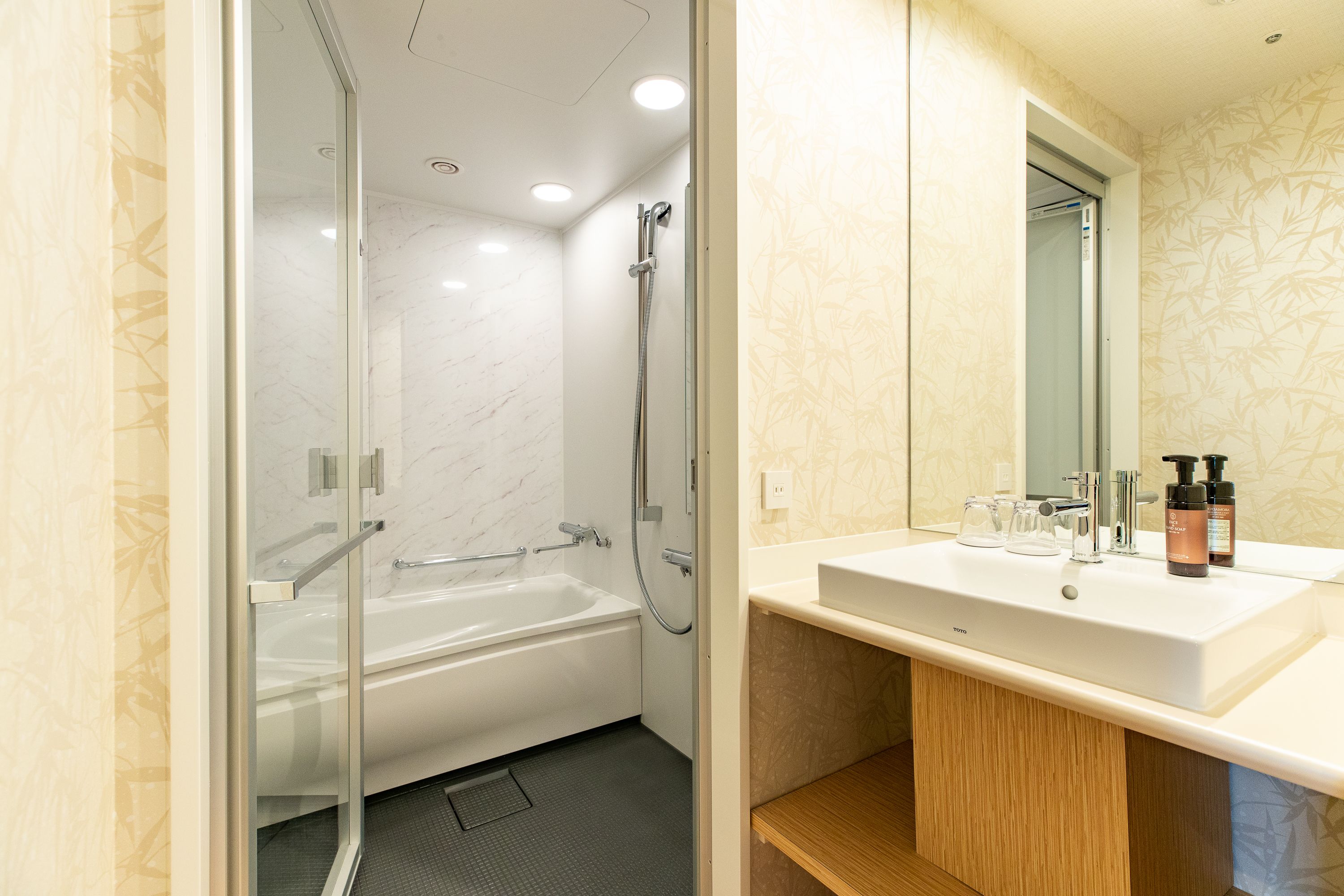 Un baño moderno con ducha envuelta en vidrio, una bañera blanca y un tocador con espejo y artículos de aseo.