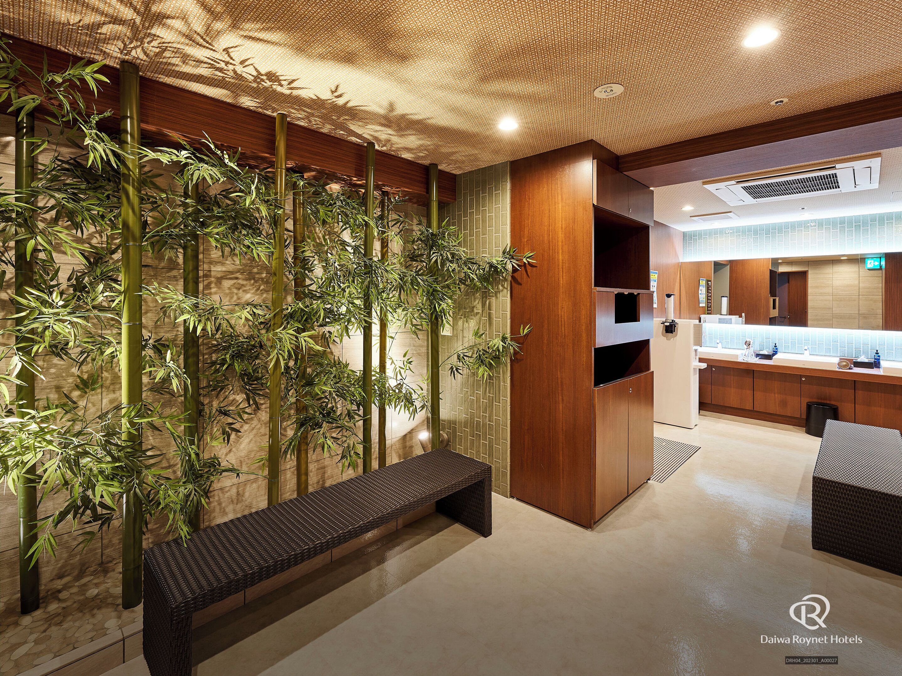 A modern hotel lobby with a bamboo wall, a seating area, and a kitchen counter.